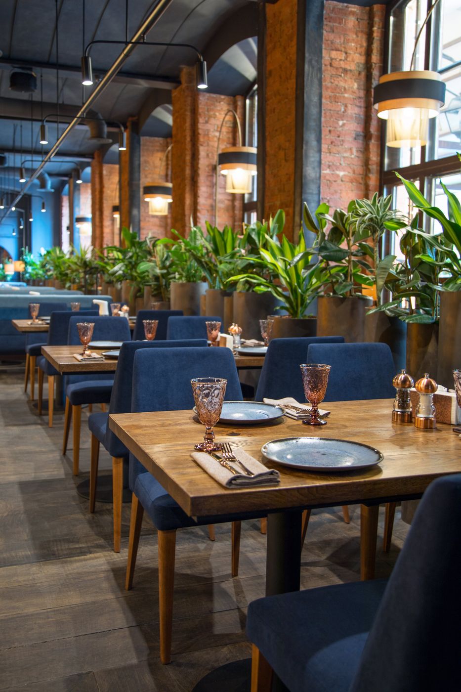 A restaurant dining room with blue chairs, brick columns and plants