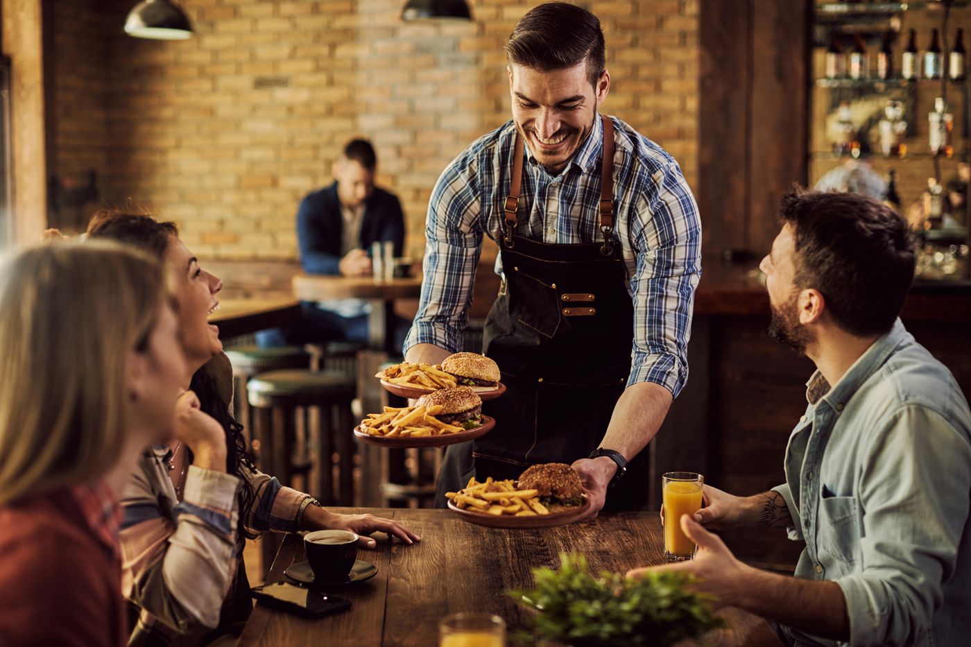 A server bringing burgers and fries to a table of friends
