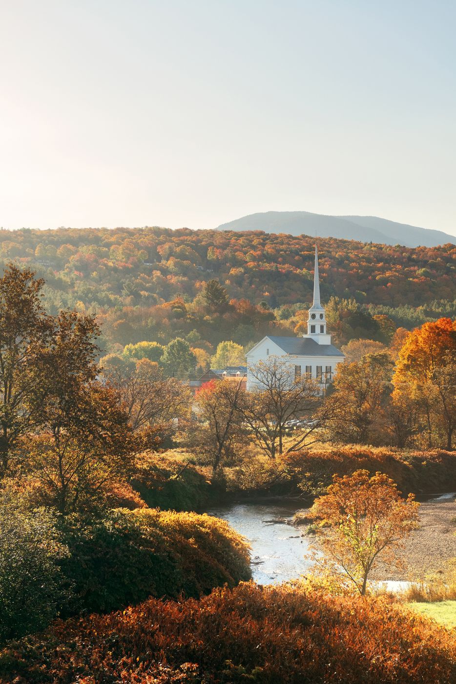 A white church steeple among autumn trees beside a stream