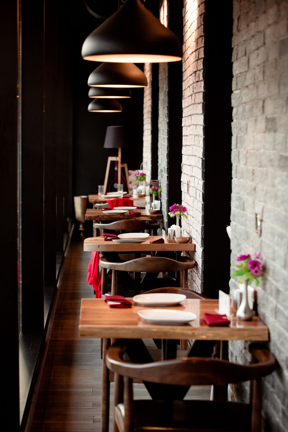 A row of small tables under black pendant lamps beside a brick wall